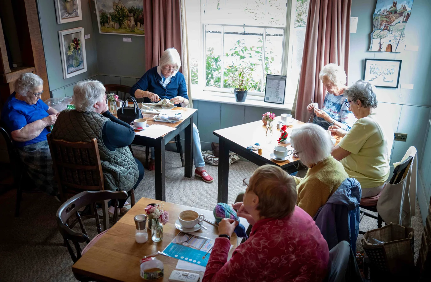 A group of women knitting and talking around tables with cups of tea in The George's community café