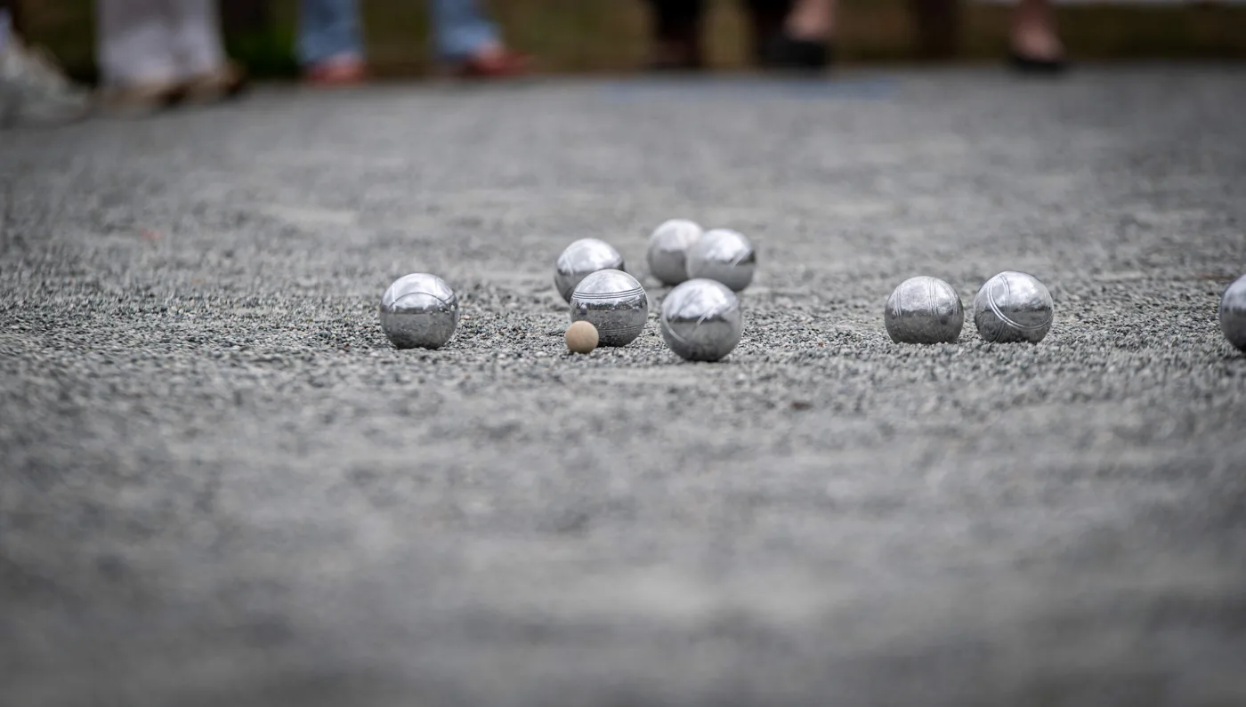 Steel boules and a small wooden jack lying on the gravel surface of the pétanque pitch