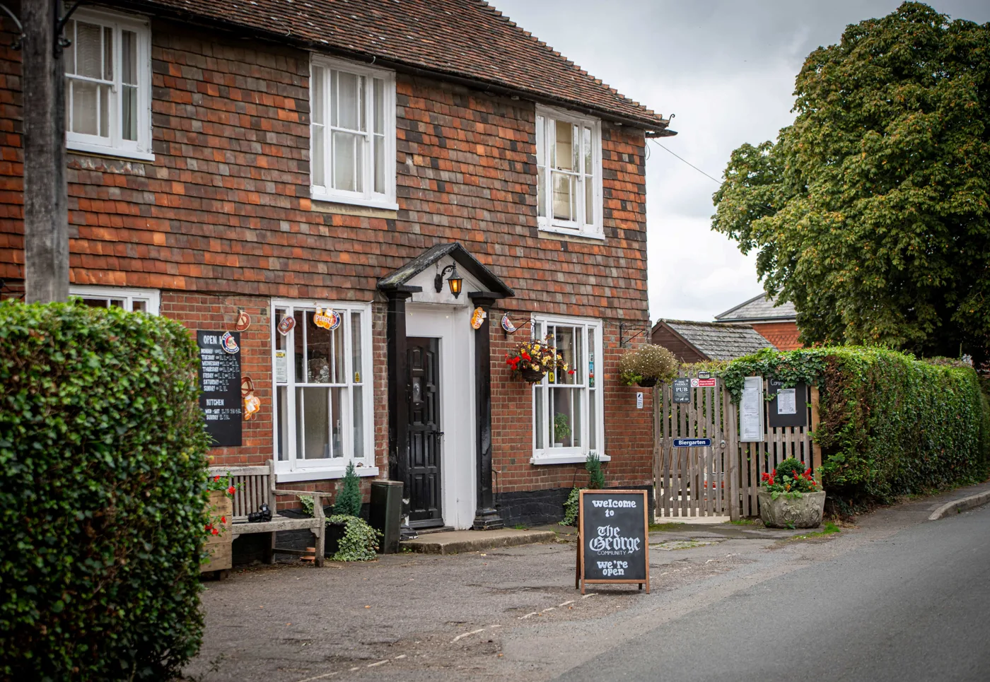 The tile-hung brick front of The George in Bethersden with a 'Welcome to The George, we're open' board on the pavement